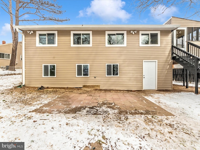 snow covered back of property with a sunroom and a patio