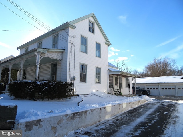 view of snow covered exterior featuring a garage, covered porch, and an outdoor structure