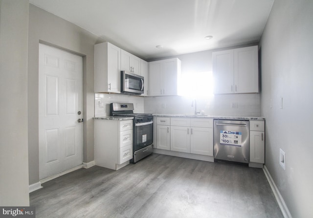 kitchen featuring appliances with stainless steel finishes, white cabinetry, light stone counters, and sink