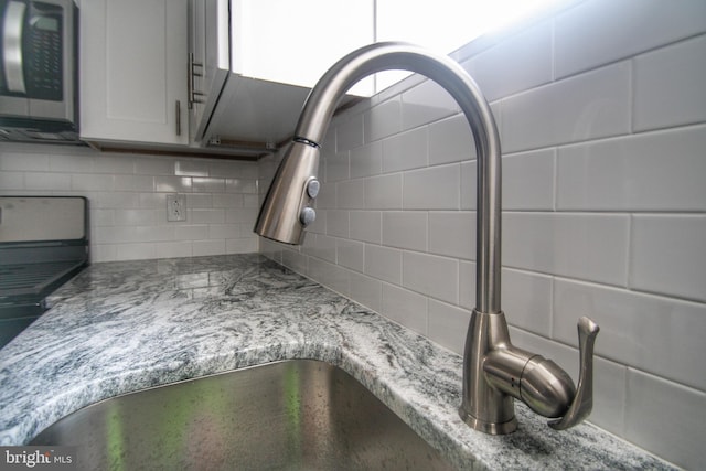 interior details with tasteful backsplash, light stone countertops, sink, and white cabinetry