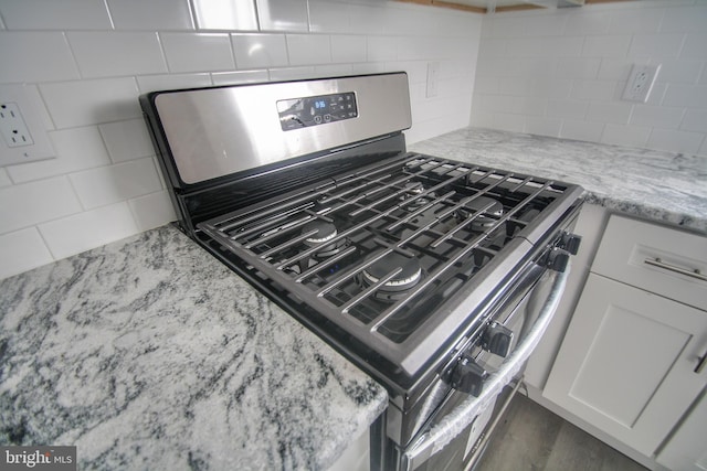 details featuring light stone counters, white cabinetry, backsplash, and stainless steel range with gas stovetop