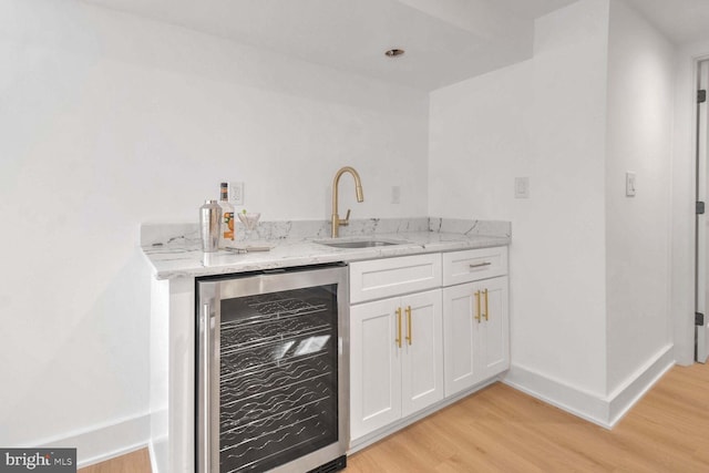 bar featuring sink, white cabinets, wine cooler, light stone countertops, and light hardwood / wood-style flooring