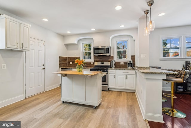 kitchen featuring light stone counters, kitchen peninsula, white cabinets, and appliances with stainless steel finishes