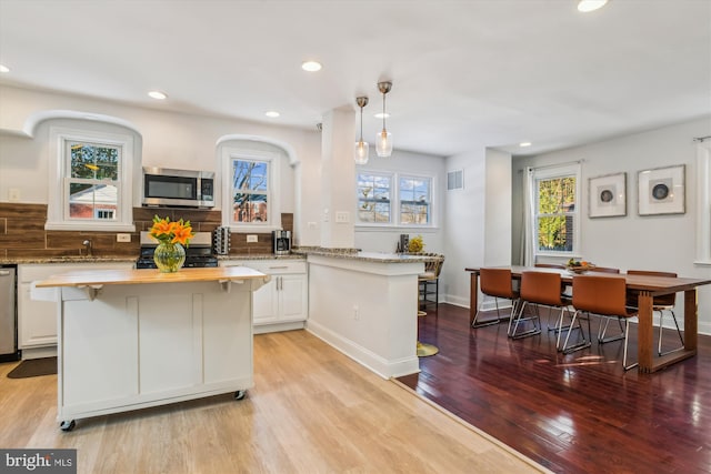 kitchen with light wood-type flooring, white cabinets, pendant lighting, stainless steel appliances, and backsplash
