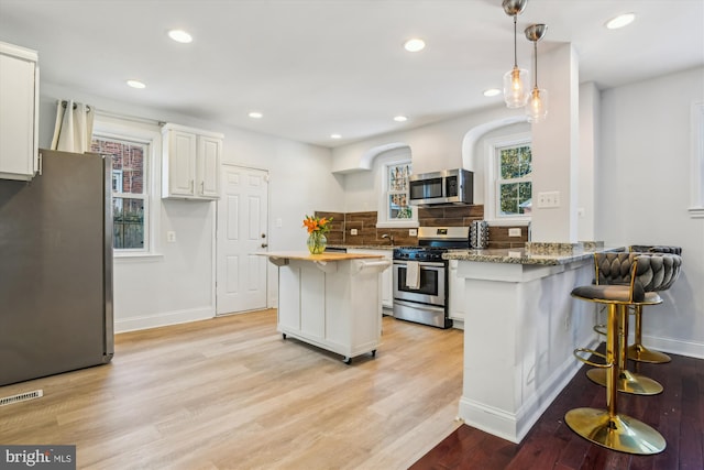 kitchen featuring appliances with stainless steel finishes, pendant lighting, dark stone countertops, white cabinets, and light hardwood / wood-style flooring