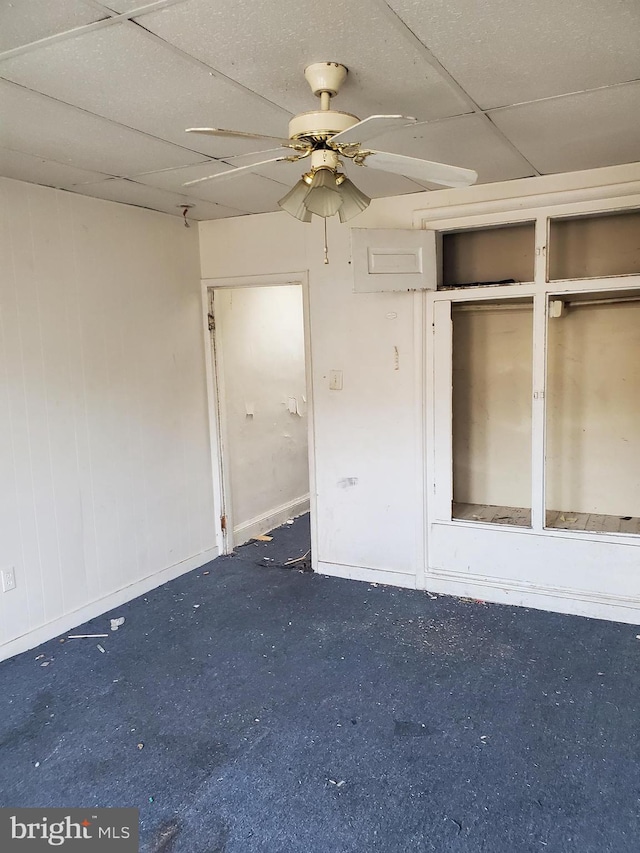 unfurnished bedroom featuring ceiling fan, two closets, a drop ceiling, and dark colored carpet