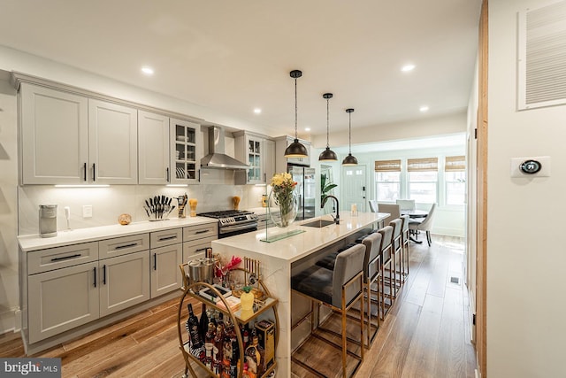 kitchen featuring an island with sink, light wood-type flooring, appliances with stainless steel finishes, and wall chimney range hood