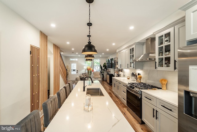 kitchen featuring appliances with stainless steel finishes, decorative light fixtures, wall chimney exhaust hood, light stone counters, and sink