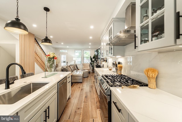 kitchen featuring stainless steel appliances, hanging light fixtures, wall chimney range hood, light hardwood / wood-style flooring, and sink