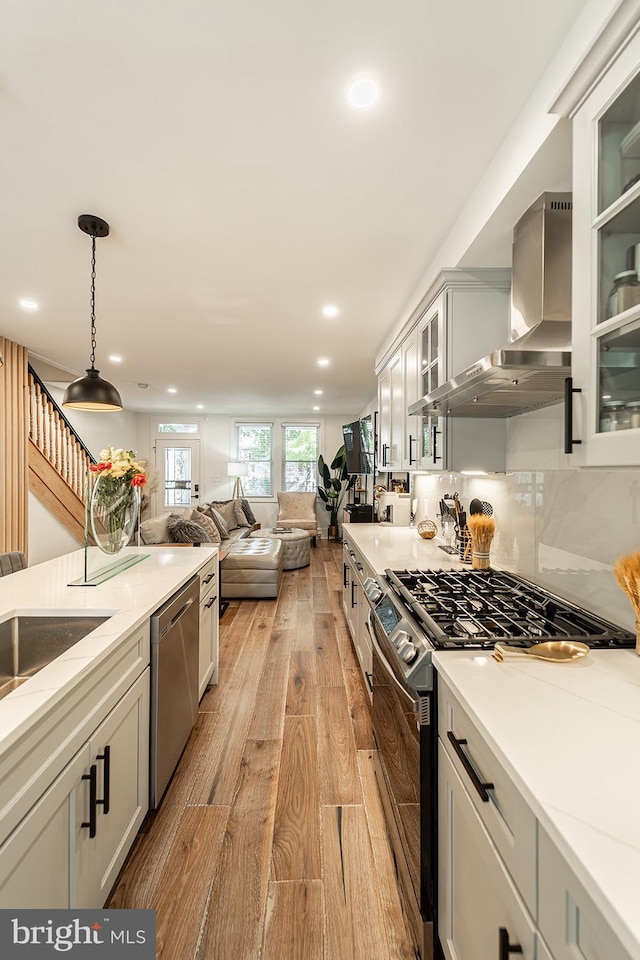 kitchen with wall chimney exhaust hood, decorative light fixtures, stainless steel appliances, decorative backsplash, and light hardwood / wood-style flooring