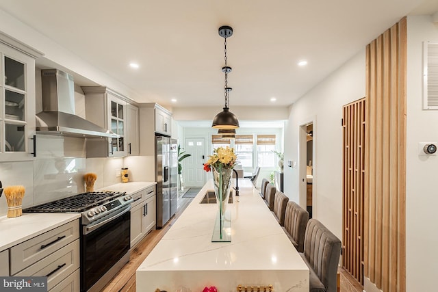 kitchen featuring gray cabinets, stainless steel appliances, decorative backsplash, wall chimney range hood, and pendant lighting