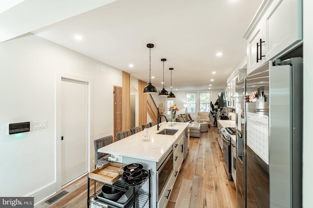 kitchen featuring decorative light fixtures, sink, light wood-type flooring, a kitchen island with sink, and white cabinets