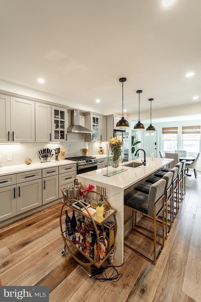 kitchen with a center island with sink, gas range, wall chimney range hood, light hardwood / wood-style flooring, and sink