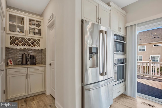 kitchen with appliances with stainless steel finishes, light hardwood / wood-style floors, and decorative backsplash