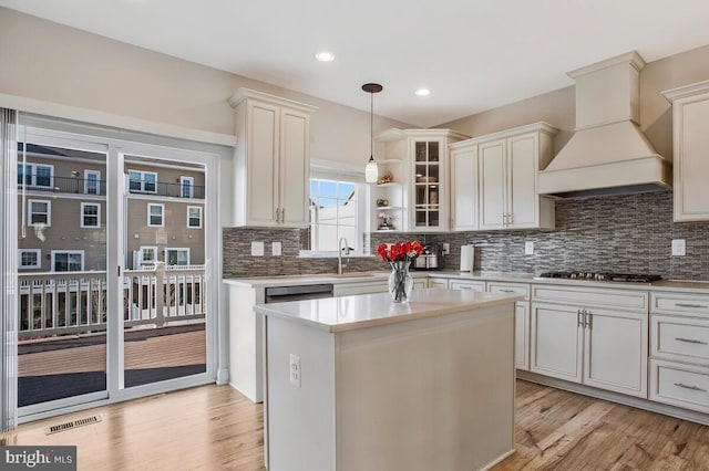 kitchen with sink, a center island, light hardwood / wood-style flooring, custom range hood, and pendant lighting