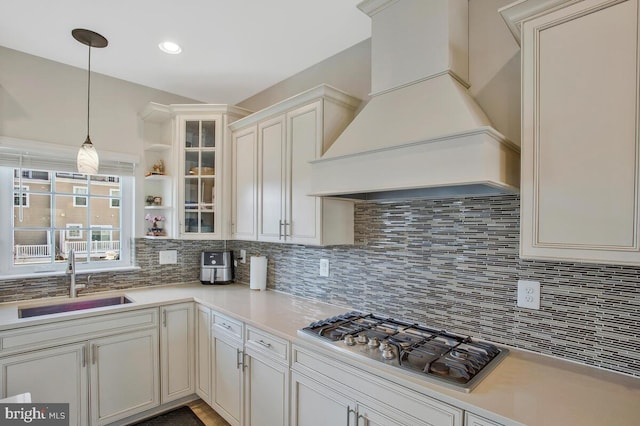 kitchen with pendant lighting, sink, backsplash, stainless steel gas cooktop, and custom exhaust hood