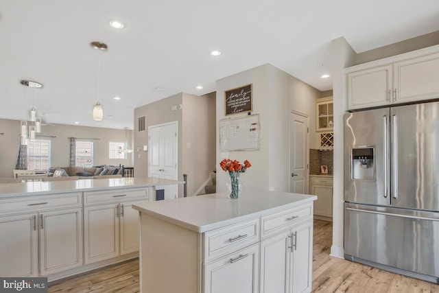 kitchen featuring stainless steel refrigerator with ice dispenser, tasteful backsplash, decorative light fixtures, a center island, and light hardwood / wood-style floors