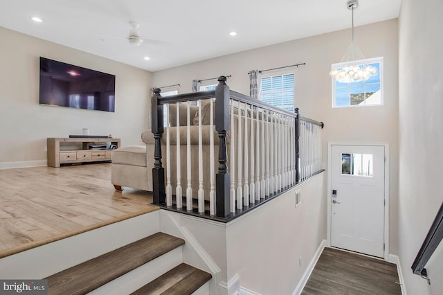 stairs featuring ceiling fan with notable chandelier and hardwood / wood-style floors