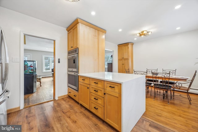 kitchen with a baseboard radiator, stainless steel double oven, light brown cabinets, kitchen peninsula, and light wood-type flooring