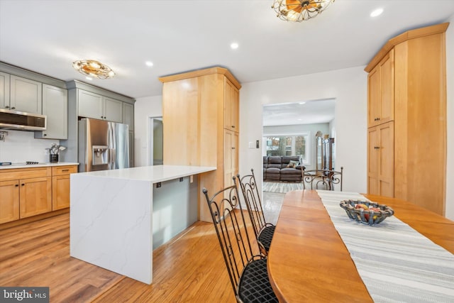 kitchen with light hardwood / wood-style floors, gray cabinets, stainless steel fridge with ice dispenser, gas stovetop, and range hood