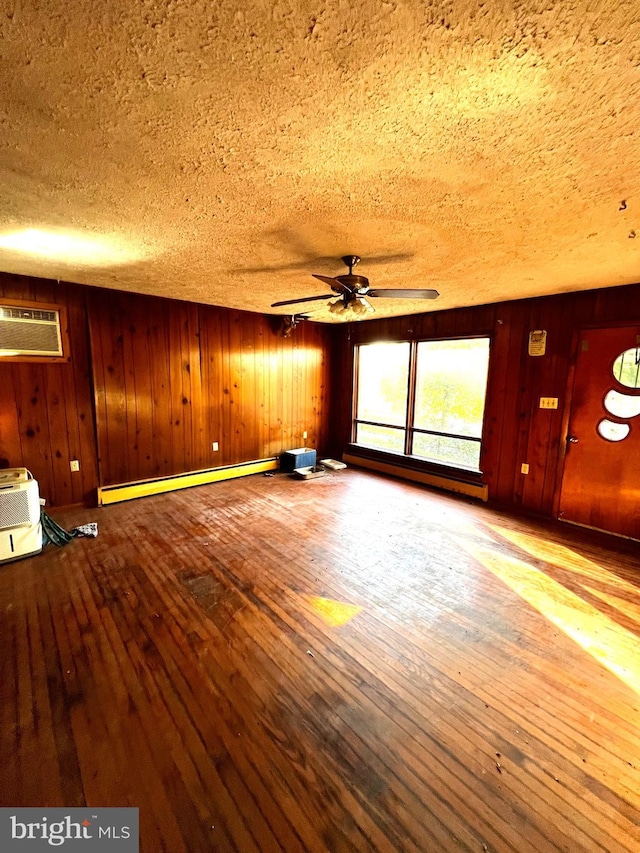 unfurnished living room featuring a wall unit AC, baseboard heating, wood-type flooring, and wood walls