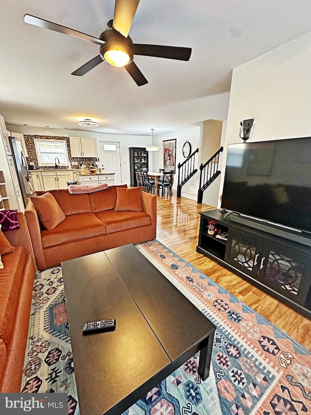 living area featuring stairs, a ceiling fan, and wood finished floors