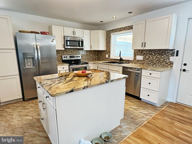 kitchen featuring decorative backsplash, a kitchen island, appliances with stainless steel finishes, white cabinetry, and a sink