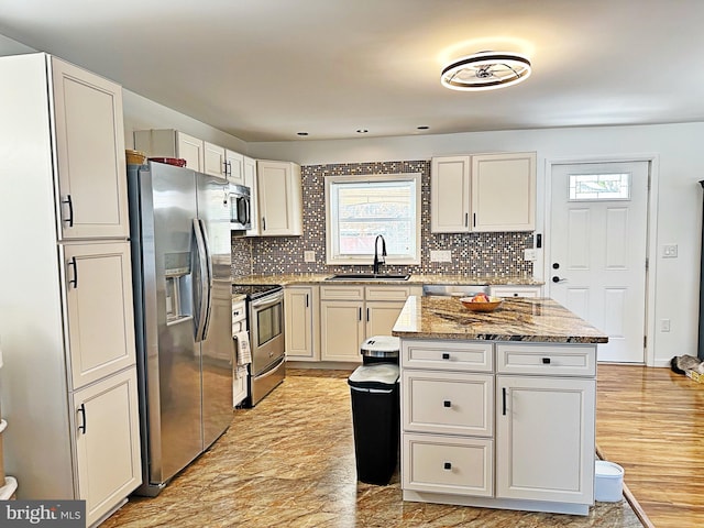 kitchen with light stone countertops, appliances with stainless steel finishes, backsplash, and a sink