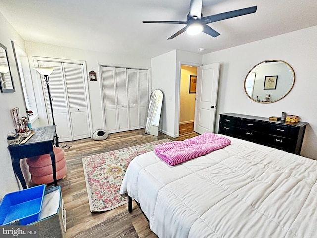 bedroom featuring multiple closets, a ceiling fan, baseboards, and wood finished floors