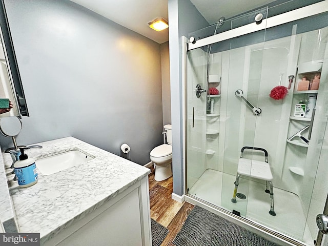 bathroom featuring toilet, vanity, a shower stall, wood finished floors, and baseboards