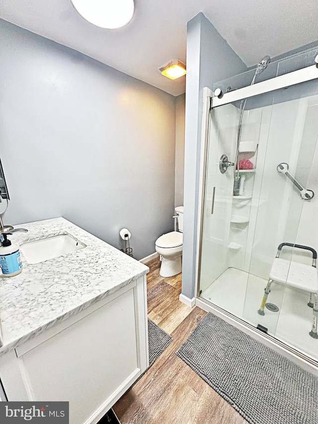 full bathroom with toilet, a stall shower, wood finished floors, and vanity