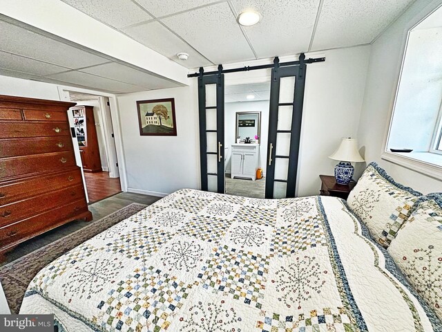 bedroom featuring a paneled ceiling, wood finished floors, baseboards, and a barn door