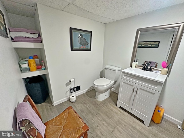 half bath with baseboards, toilet, wood finished floors, vanity, and a paneled ceiling