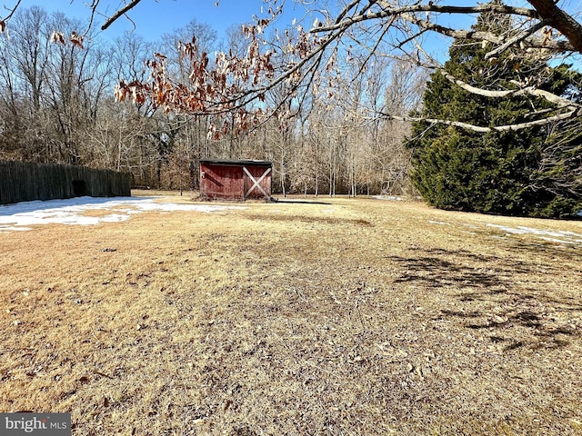 view of yard with fence, a view of trees, and an outdoor structure