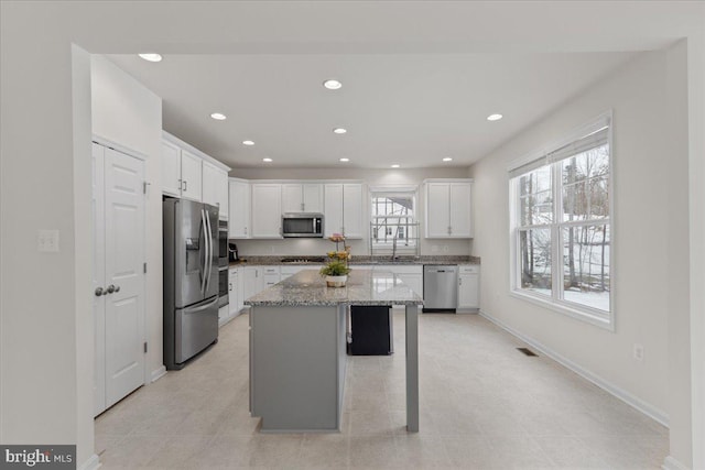 kitchen with light stone countertops, white cabinets, a center island, stainless steel appliances, and a kitchen breakfast bar