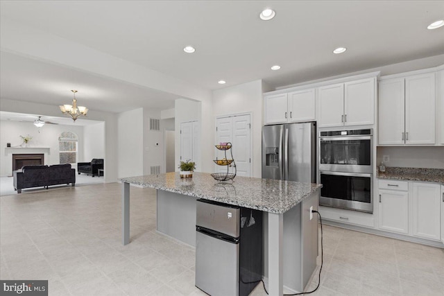 kitchen featuring appliances with stainless steel finishes, white cabinets, light stone counters, and a center island