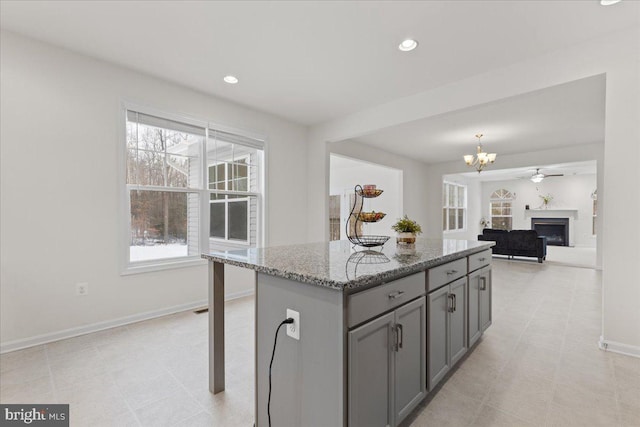 kitchen featuring stone counters, gray cabinets, a center island, a kitchen breakfast bar, and ceiling fan with notable chandelier