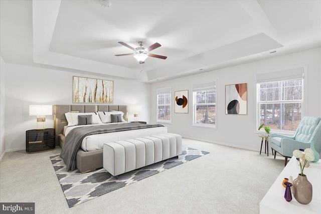 carpeted bedroom featuring ceiling fan and a raised ceiling