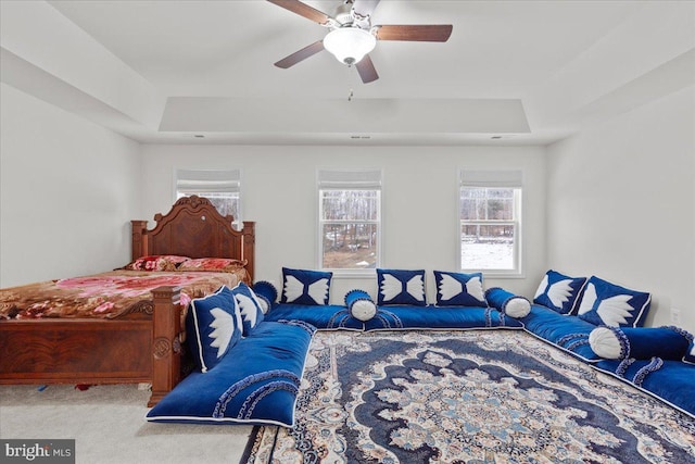 carpeted bedroom with ceiling fan and a tray ceiling