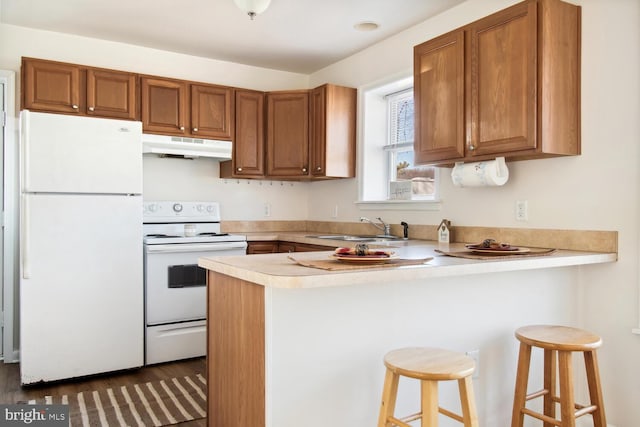 kitchen with a kitchen bar, sink, dark hardwood / wood-style floors, kitchen peninsula, and white appliances