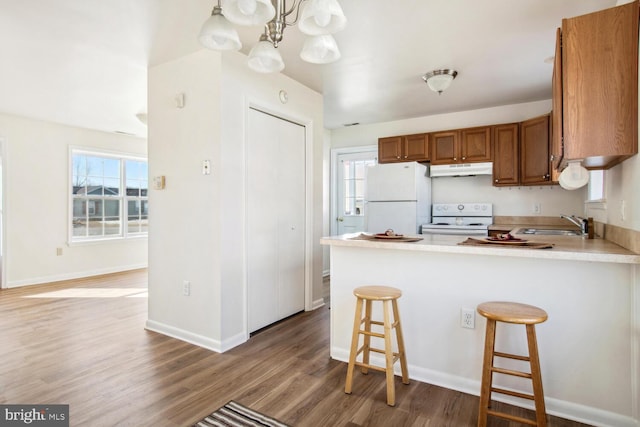 kitchen featuring a breakfast bar, wood-type flooring, decorative light fixtures, kitchen peninsula, and white appliances