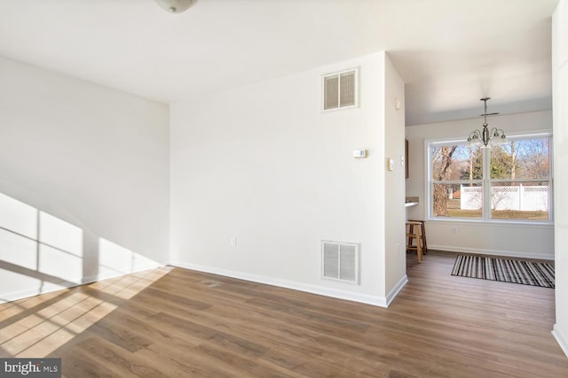 spare room with an inviting chandelier and hardwood / wood-style floors