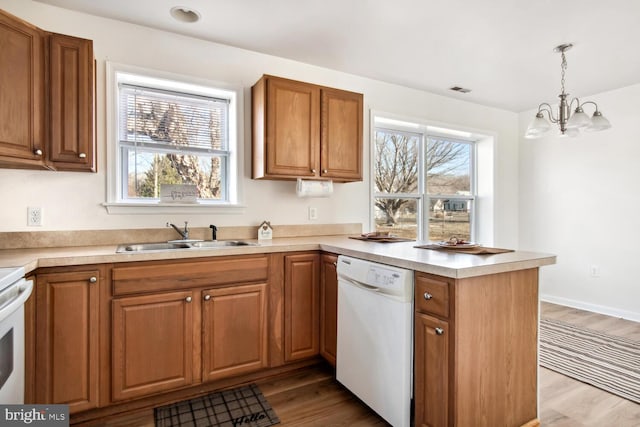 kitchen with decorative light fixtures, dishwasher, sink, kitchen peninsula, and light hardwood / wood-style flooring