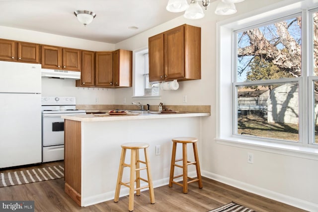 kitchen featuring a kitchen bar, a notable chandelier, kitchen peninsula, dark wood-type flooring, and white appliances