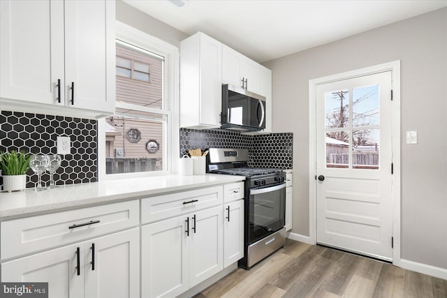 kitchen featuring appliances with stainless steel finishes, backsplash, light wood-type flooring, light stone countertops, and white cabinets