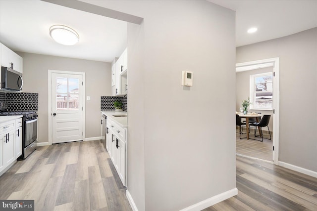 kitchen featuring appliances with stainless steel finishes, light hardwood / wood-style floors, backsplash, and white cabinets