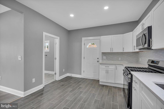 kitchen featuring appliances with stainless steel finishes, white cabinetry, backsplash, light wood-type flooring, and light stone counters