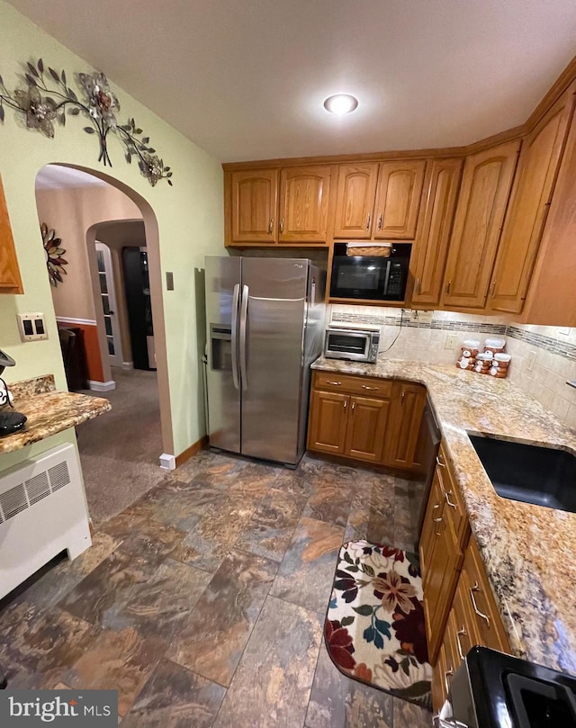 kitchen featuring sink, stainless steel fridge, backsplash, range, and light stone countertops