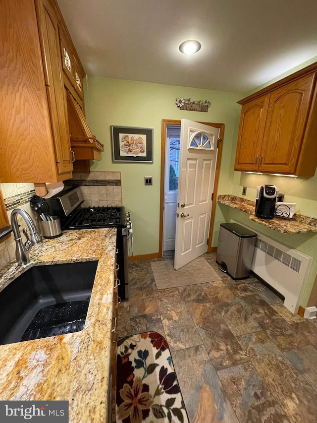 kitchen featuring sink, radiator, light stone countertops, and stainless steel range with gas stovetop