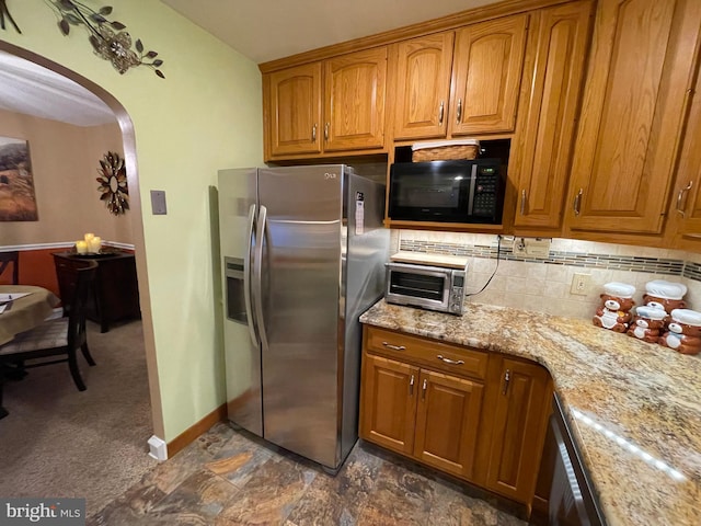 kitchen featuring light stone counters, backsplash, stainless steel fridge, and dishwasher